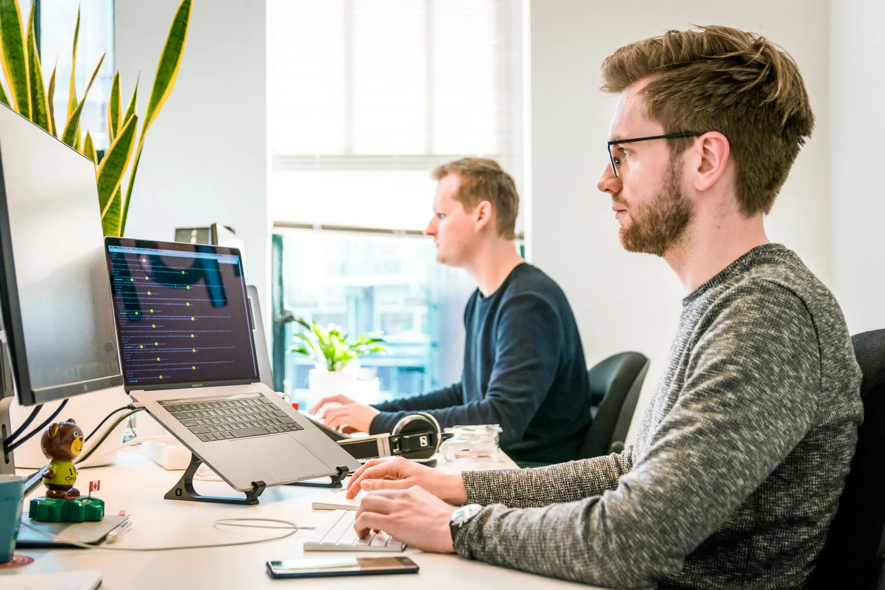 Two developers working side by side at large monitors in a bright office
