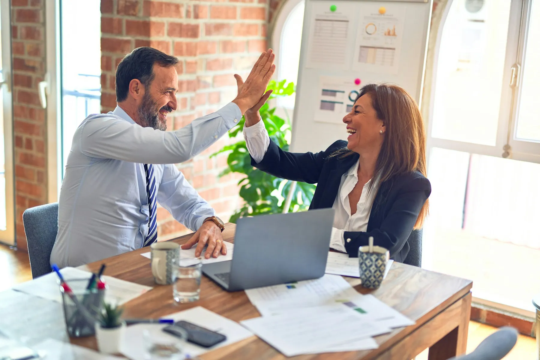 Two colleagues celebrating at a desk in a bright office